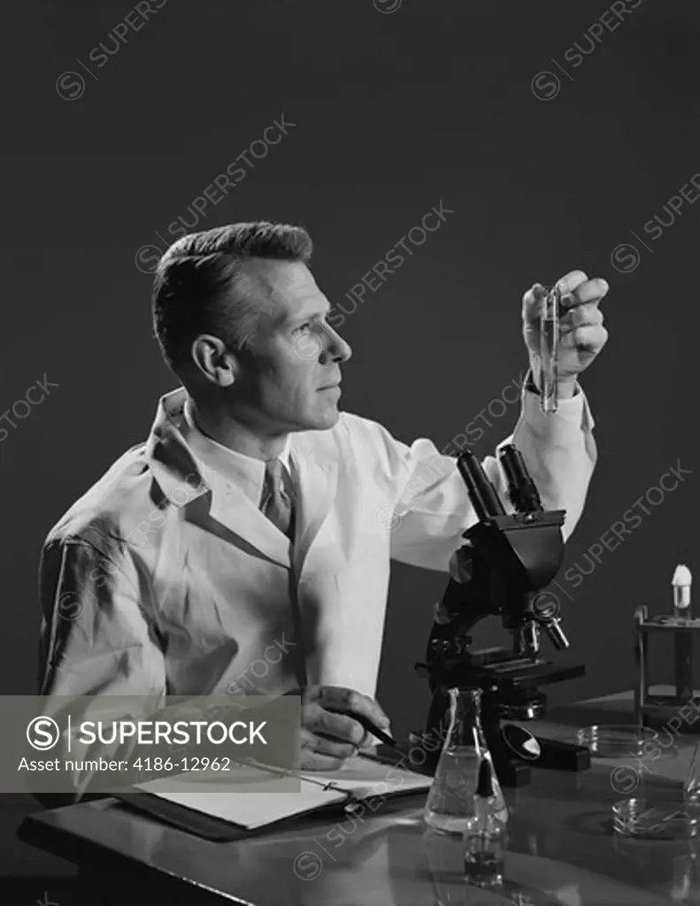 1950S Man Scientist Holding Test Tube Making Notes By Microscope  