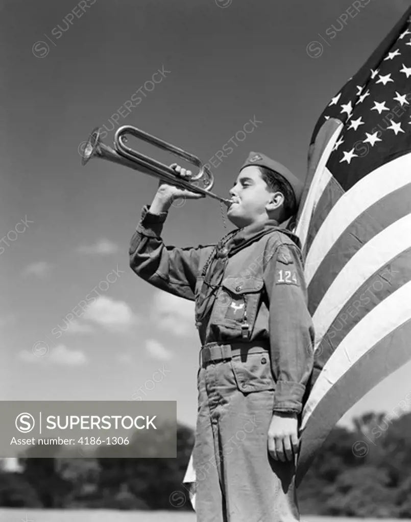 1950S Side View Of Boy Scout Standing In Front Of American Flag Bugling