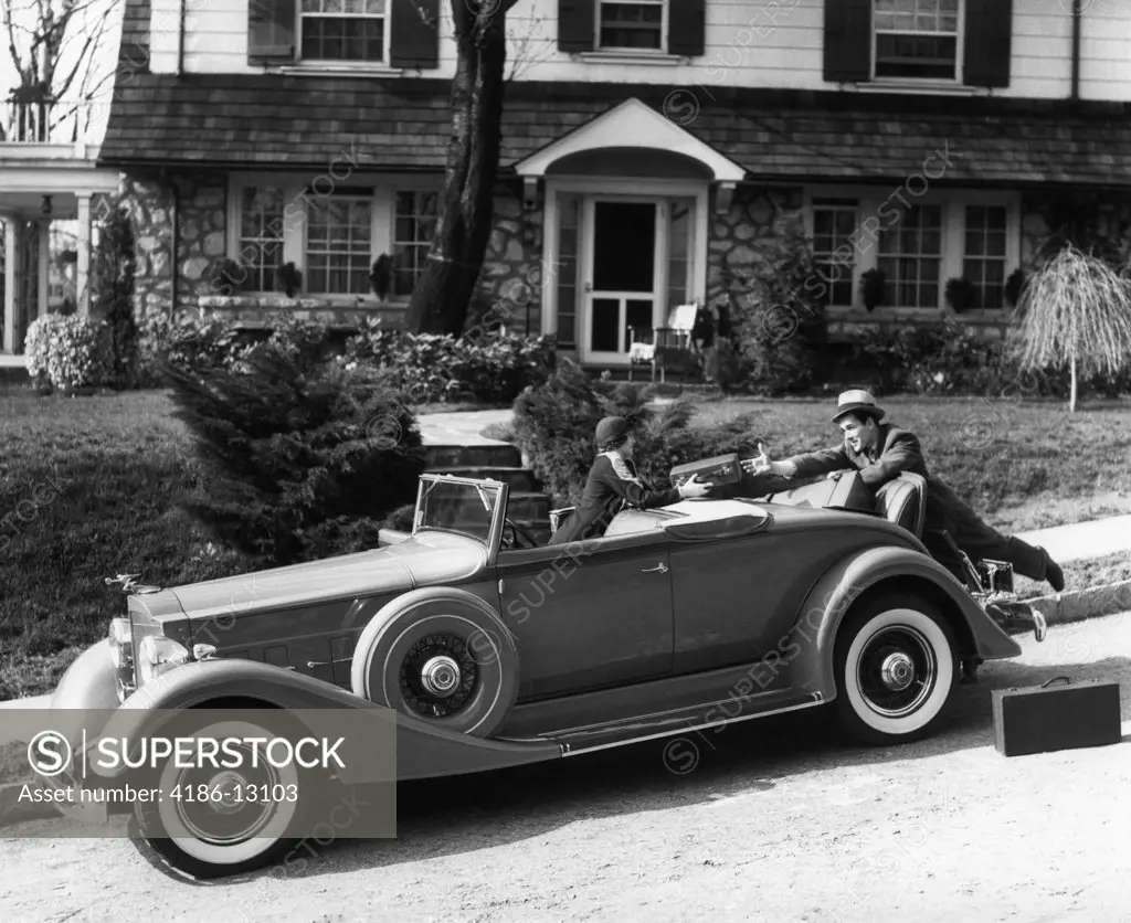 1930S Woman In Car Packard Handing Suitcase To Man In Front Of House Couple Travel Trip