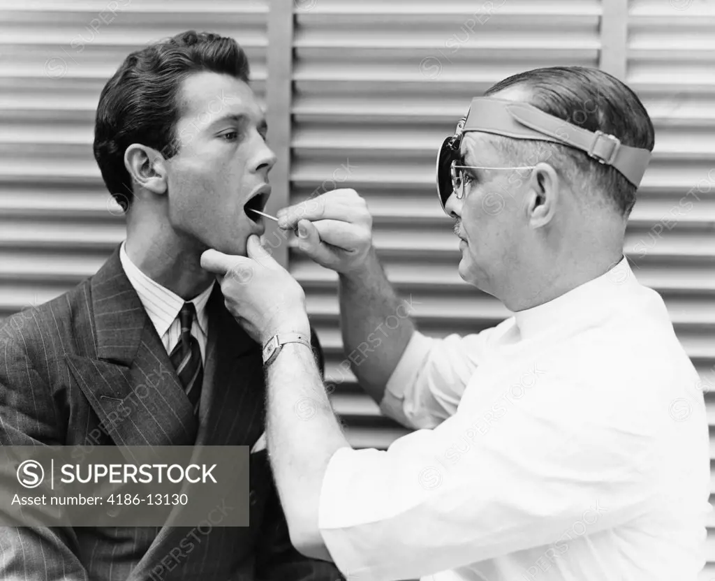 1930S 1940S Doctor Examining Throat Of Young Man Patient
