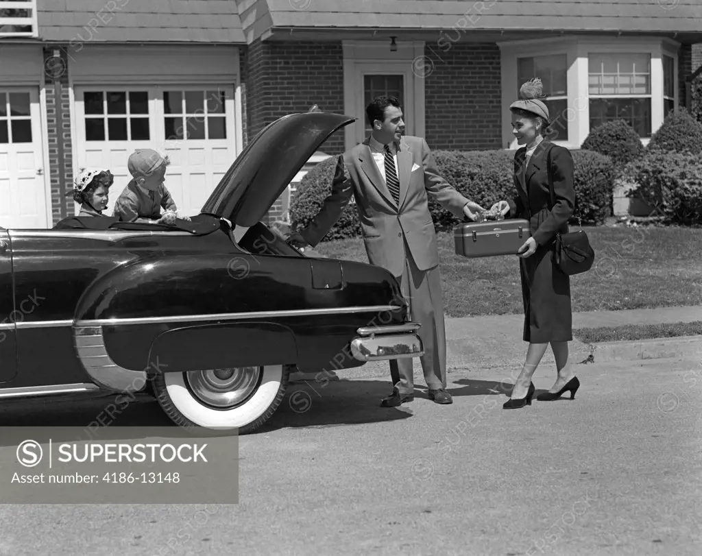 1950S Husband And Wife Packing Trunk Of Convertible With Luggage While Son & Daughter Watch From Back Seat