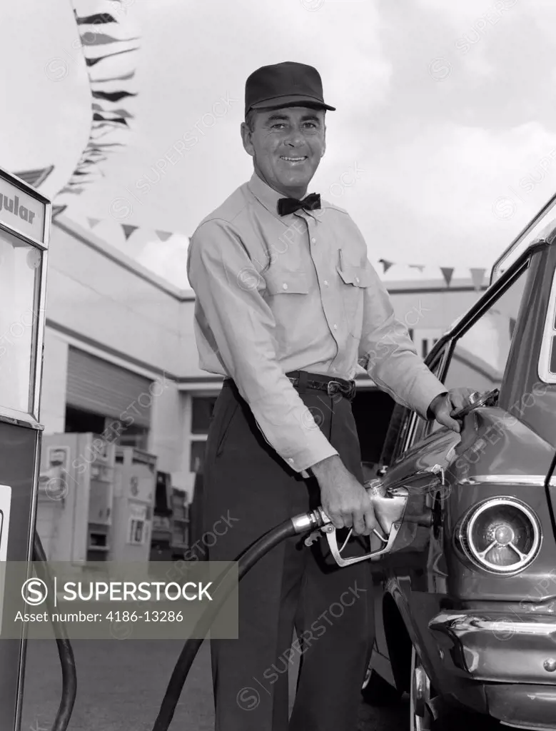 1960S Male Service Station Attendant Wearing Cap And Bow Tie Smiling While Pumping Gasoline Outside