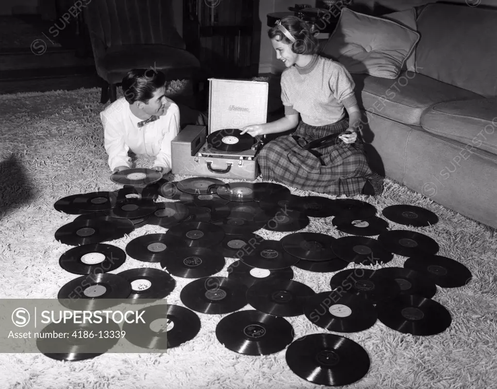 1950S Teenage Couple Playing Many Music Records Spread Out On Living Room Floor