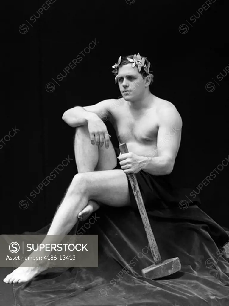 1920S Man Semi Nude Sitting Classical Pose Wearing Laurel Wreath On Head Holding Long Armed Hammer Retro Vintage