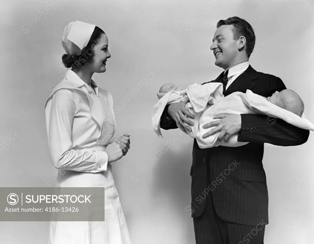 1930S 1940S Smiling Woman Nurse Talking With Man Proud New Father Holding Newborn Twin Babies