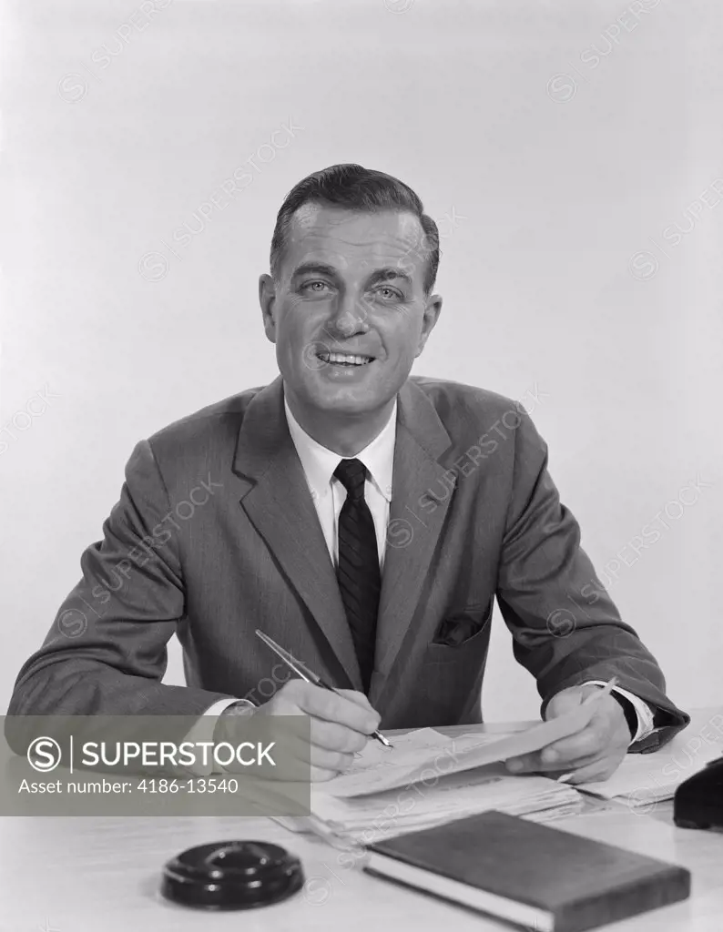 1960S Smiling Happy Businessman Pen In Hand Signing Papers At Desk