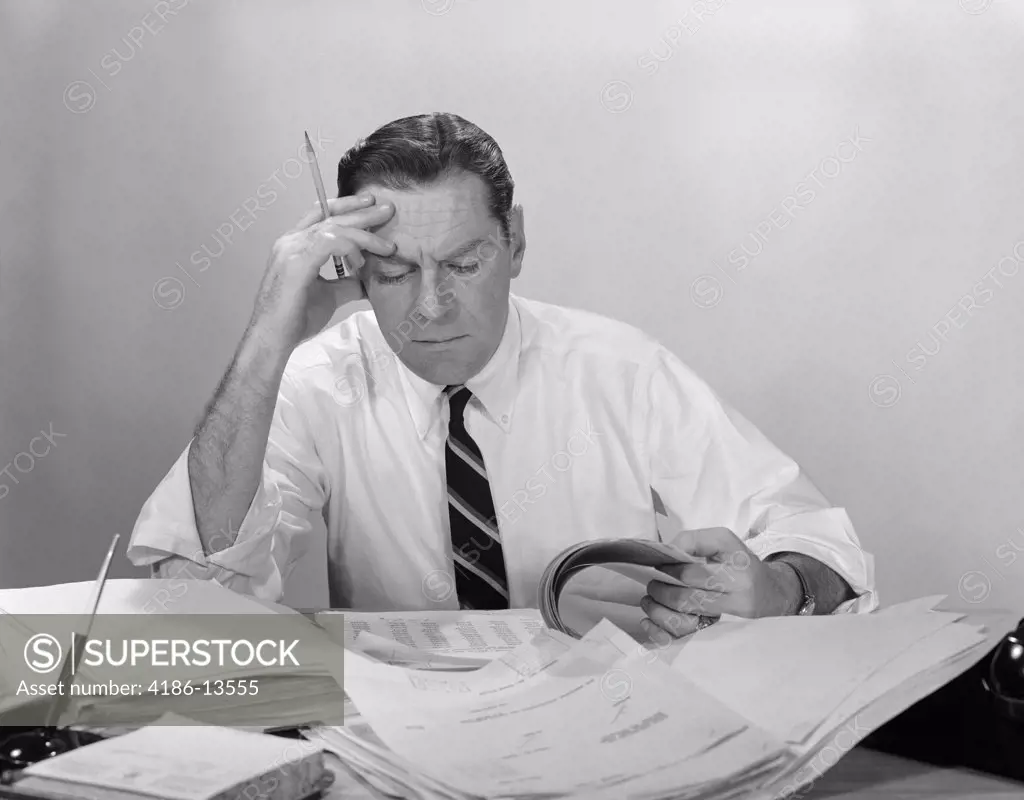 1960S Businessman Desk Full Papers Hand To Forehead Serious Expression