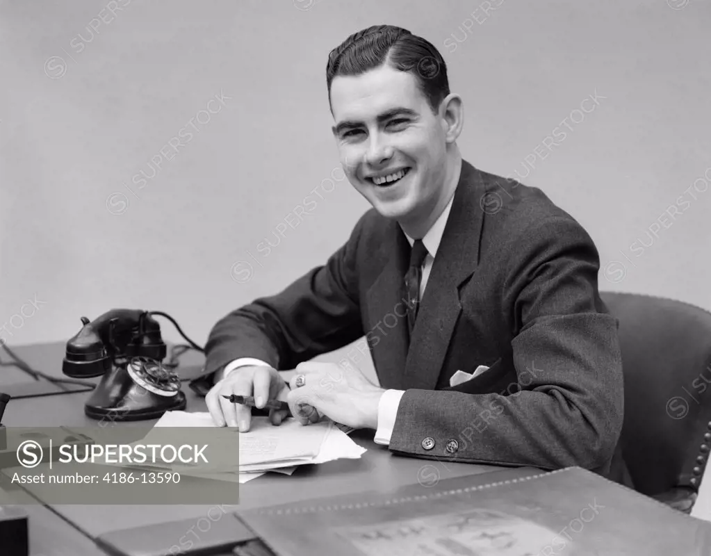 1930S Man Sitting At Desk In Office Holding Pen Smiling