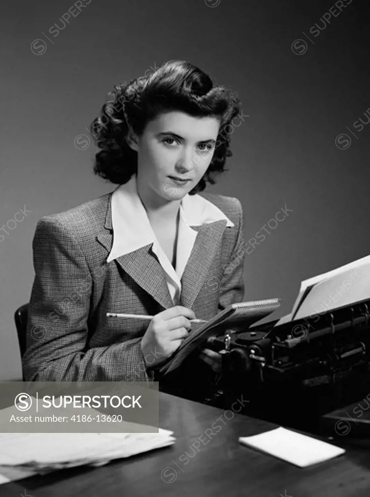 1940S Serious Secretary Stenographer Woman With Pencil Checking Notepad Sitting At Desk With Manual Typewriter Office Indoor