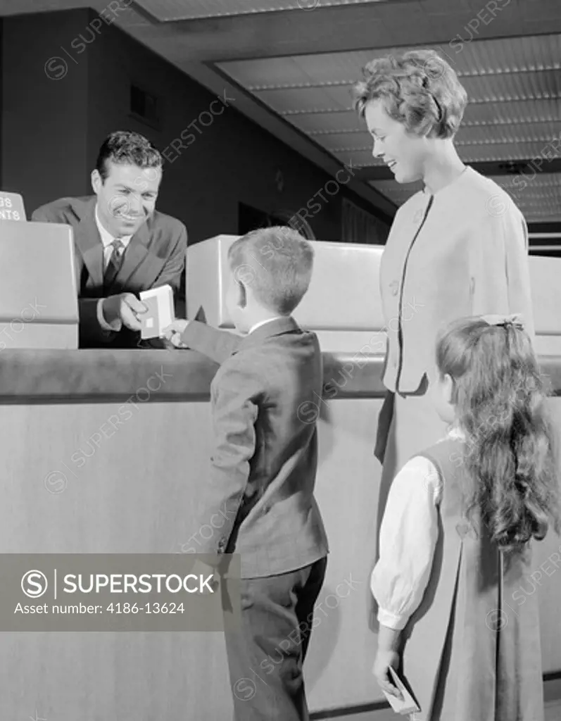 1960S Mother Two Children Boy Handing Banking Deposit To Male Bank Teller