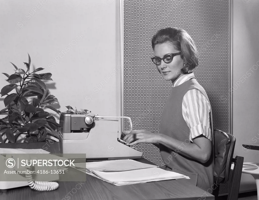 1960S Secretary Typist Wearing Stylish Eyeglasses Using Manual Typewriter At Desk