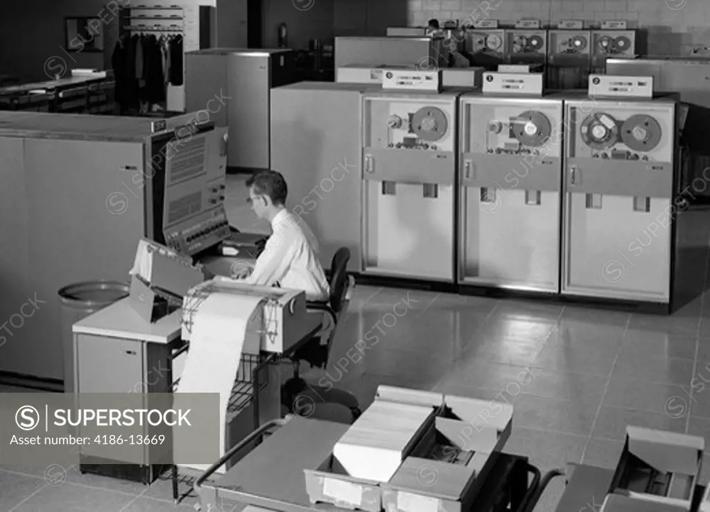 1960S Man Programming Large Mainframe Computer Surrounded By Data Tape Drives Indoor