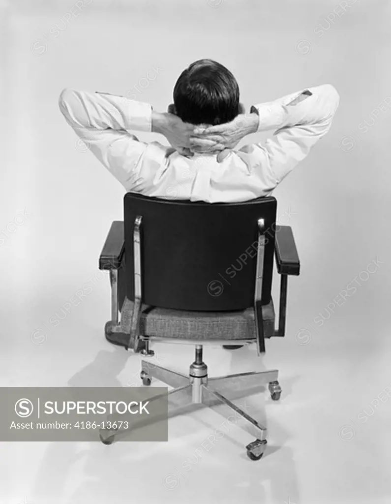 1960S Man From Behind Sitting In Office Executive Chair Hands Clasped Behind Neck