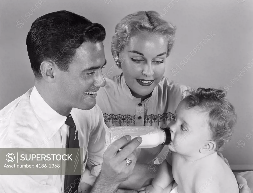 1950S Smiling Father Feeding Baby Milk From Bottle With Mother At Side