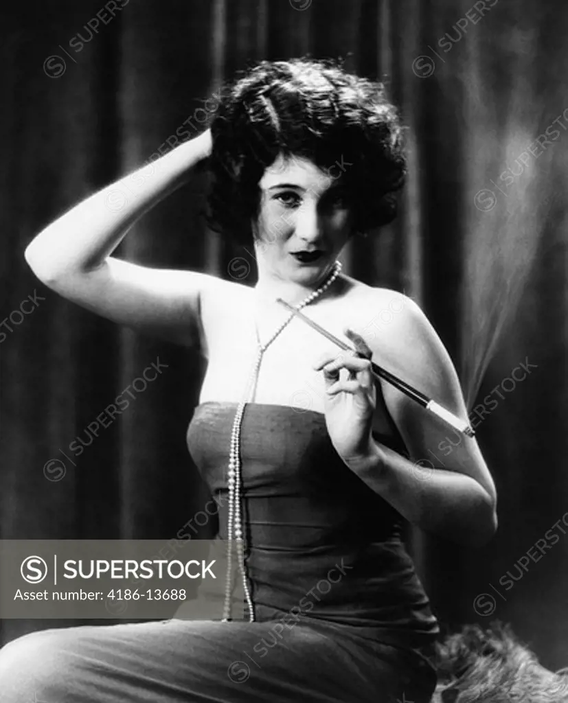 1920S Woman Wearing Strapless Gown And String Of Pearls Holding Long Cigarette Holder With Other Hand On Back Of Head