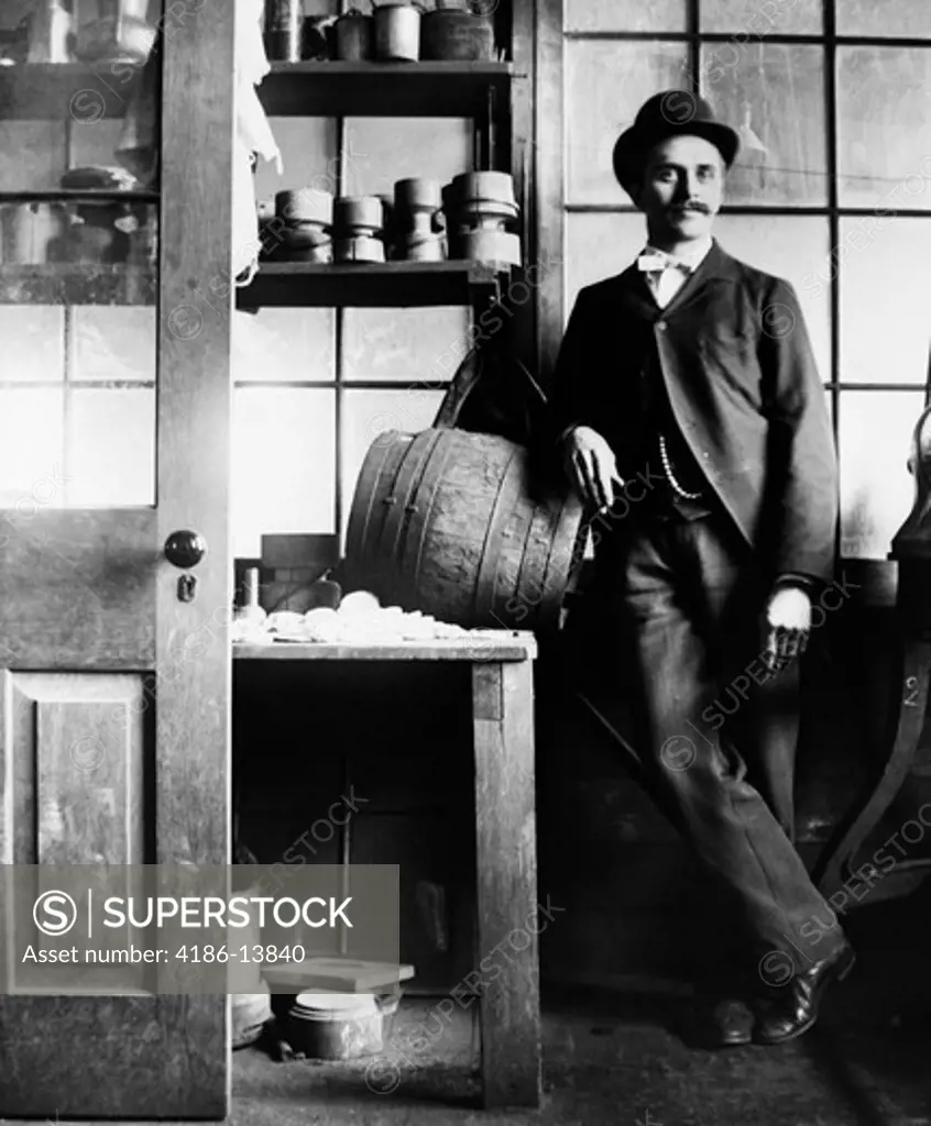1890S 1900S Turn Of The Century Man In Suit & Bowler Leaning On Wooden Barrel On Table
