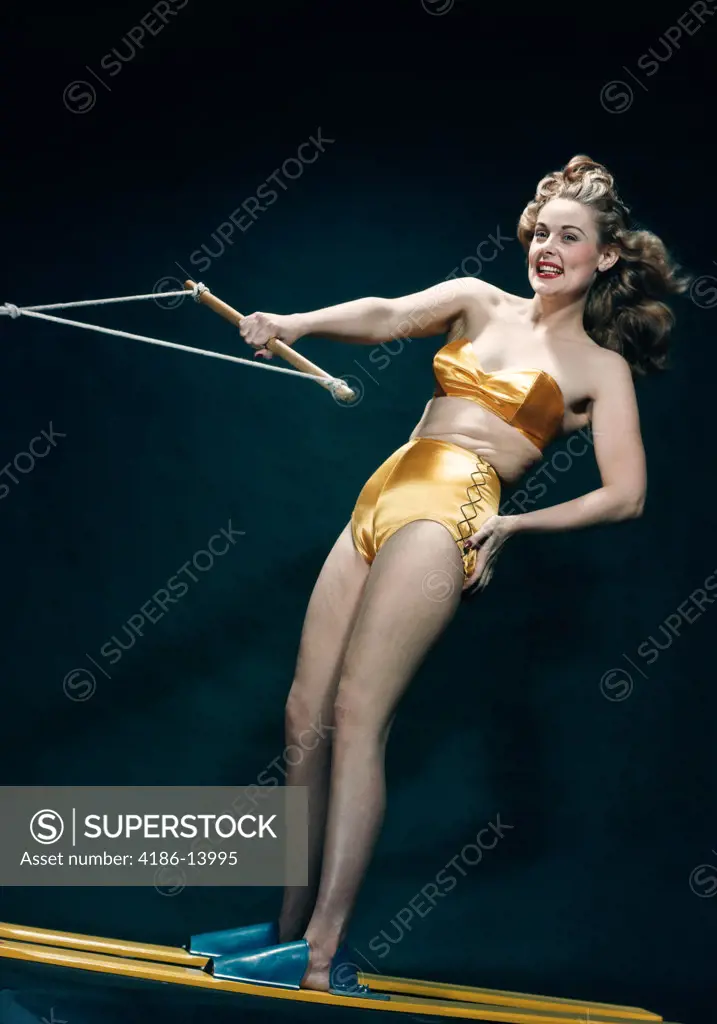 1950S Smiling Woman Pinup Wearing Two Piece Gold Bikini Bathing Suit Posing Riding Water Skis Indoors