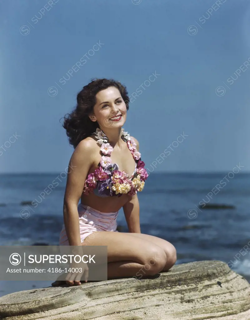 1940S 1950S Smiling Brunette Woman Sitting On Rock Wearing Two Piece Bathing Suit Appliquéd With Pastel Flowers