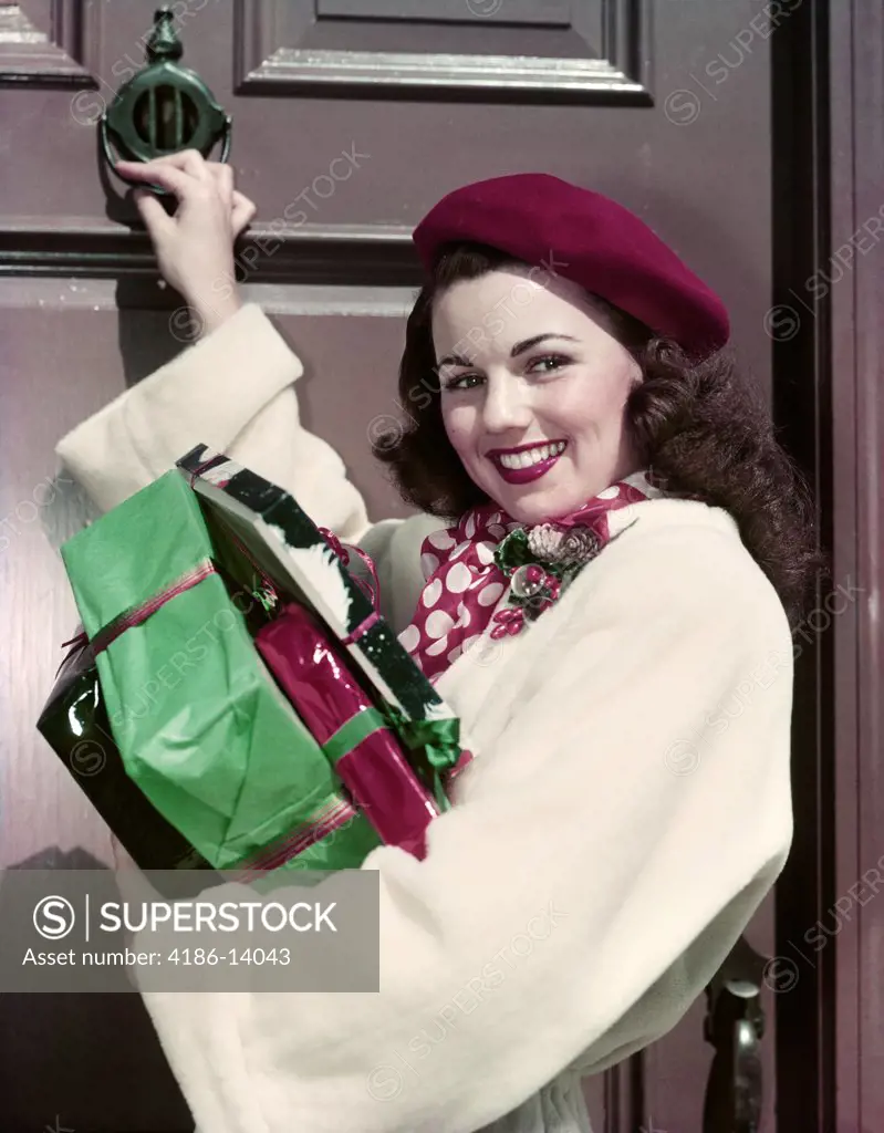 1950S Smiling Woman Carrying Christmas Presents Knocking On House Door