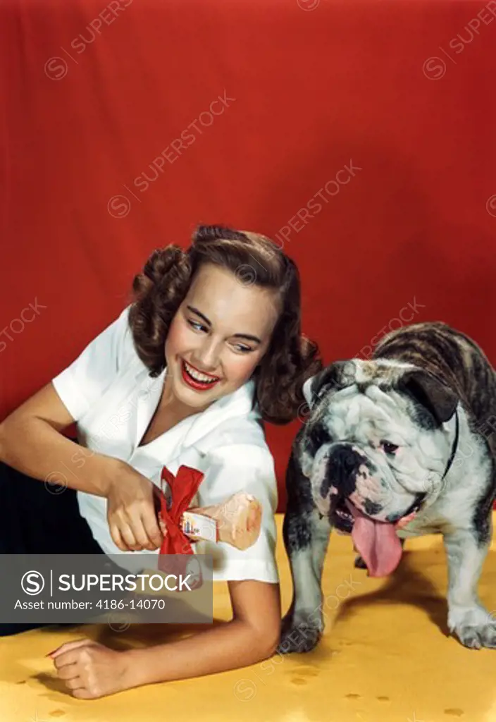 1940S 1950S Young Woman Giving Bulldog A Present Of A Bone Wrapped In Red Bow