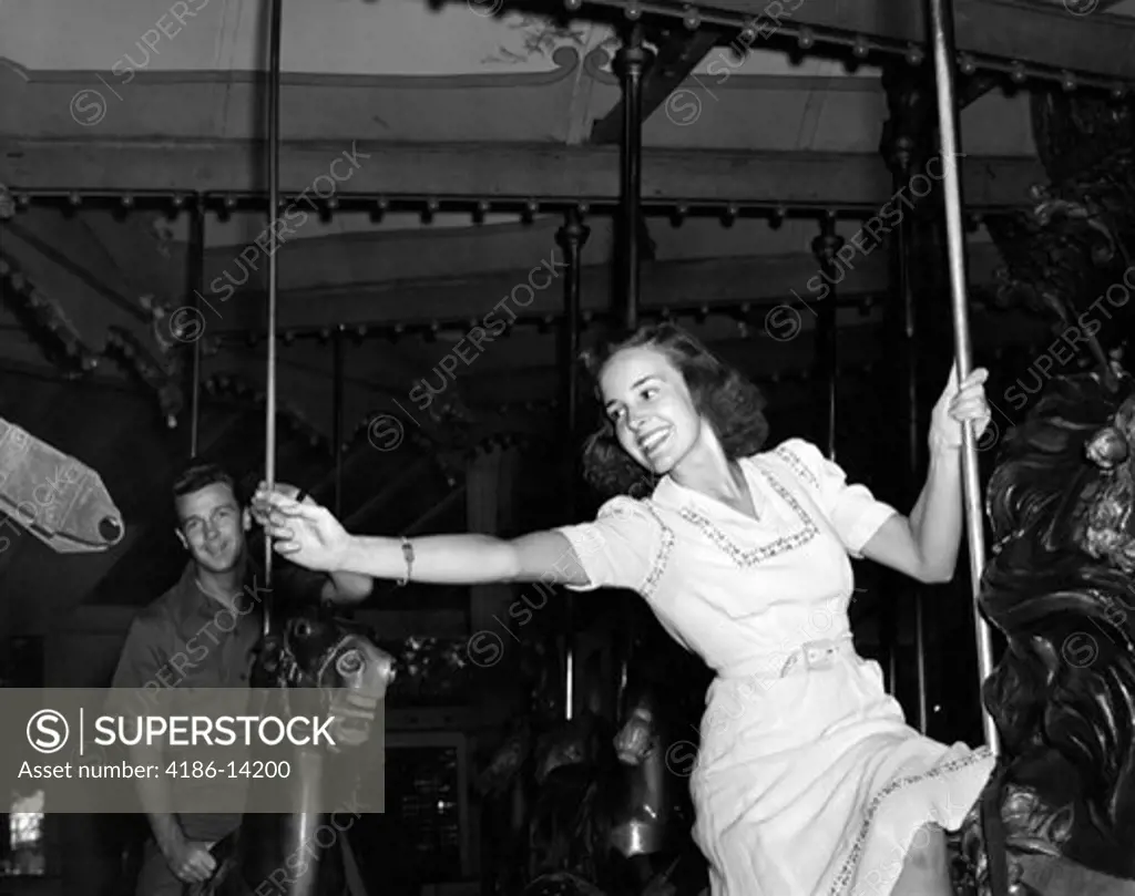 1940S Woman On Carousel Reaching For Brass Ring Man In Background Indoor