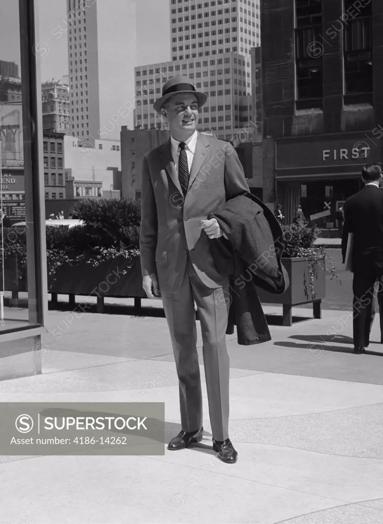 1950S 1960S Businessman Wearing Suit Hat Carrying Top Coat Standing On City Street 