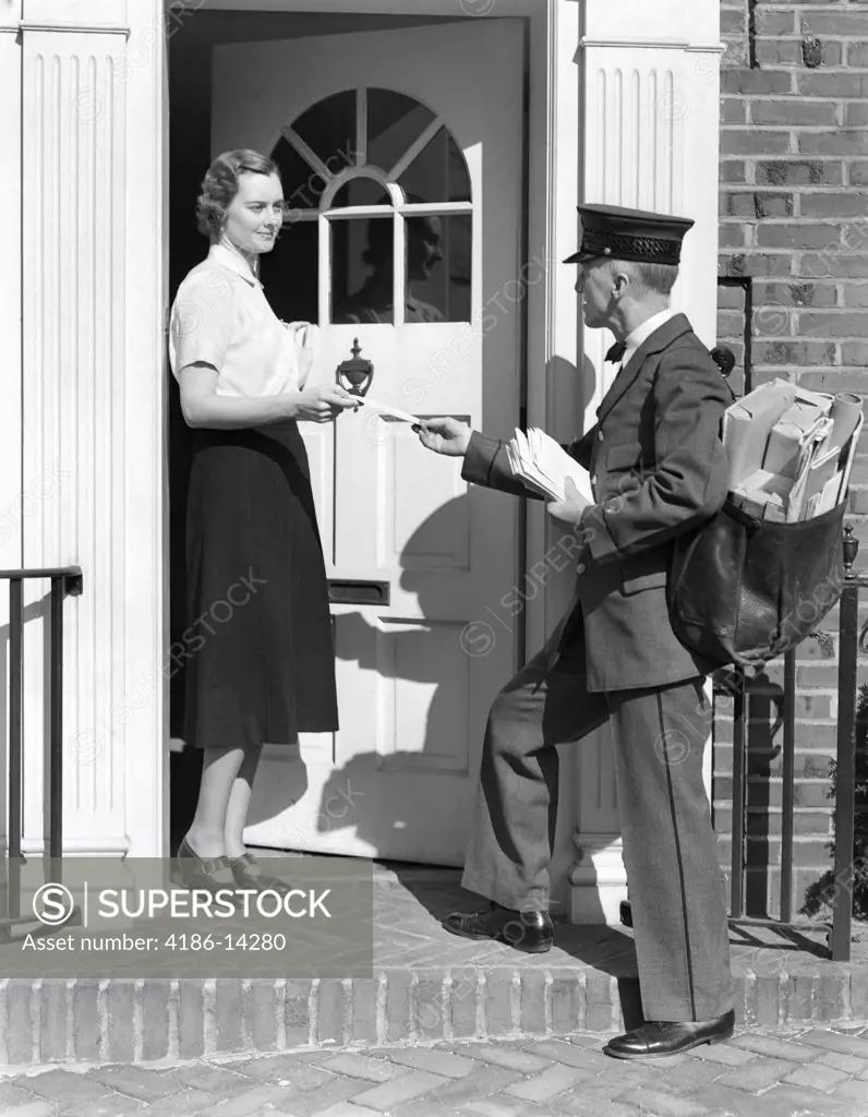 1930S Postman Giving A Letter To A Woman In The Doorway Of A Colonial Brick Home