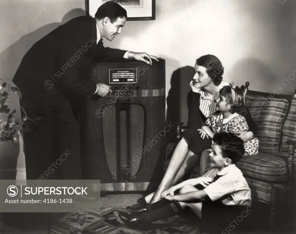1930S Family Listening To Radio Father Tuning Channel Mother Children Sitting Couch