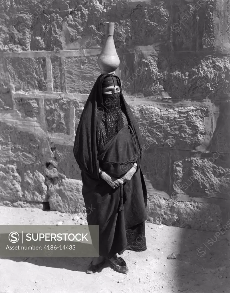 1920S 1930S Egyptian Woman With Pitcher Balanced On Head Wearing Traditional Arab Muslim Garb Face Veiled