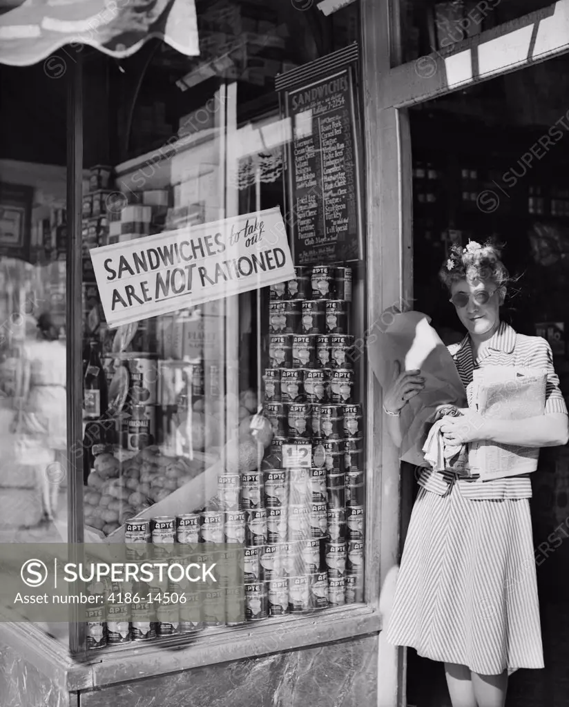 1940S Woman Carrying Packages In Door Of New York City Delicatessen Displaying A Sign Sandwiches To Take Out Are Not Rationed