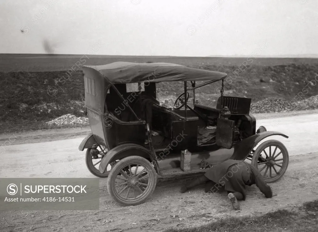 1920S 1930S Man On His Hands And Knees Looking Under Model T Broken Down On Roadside