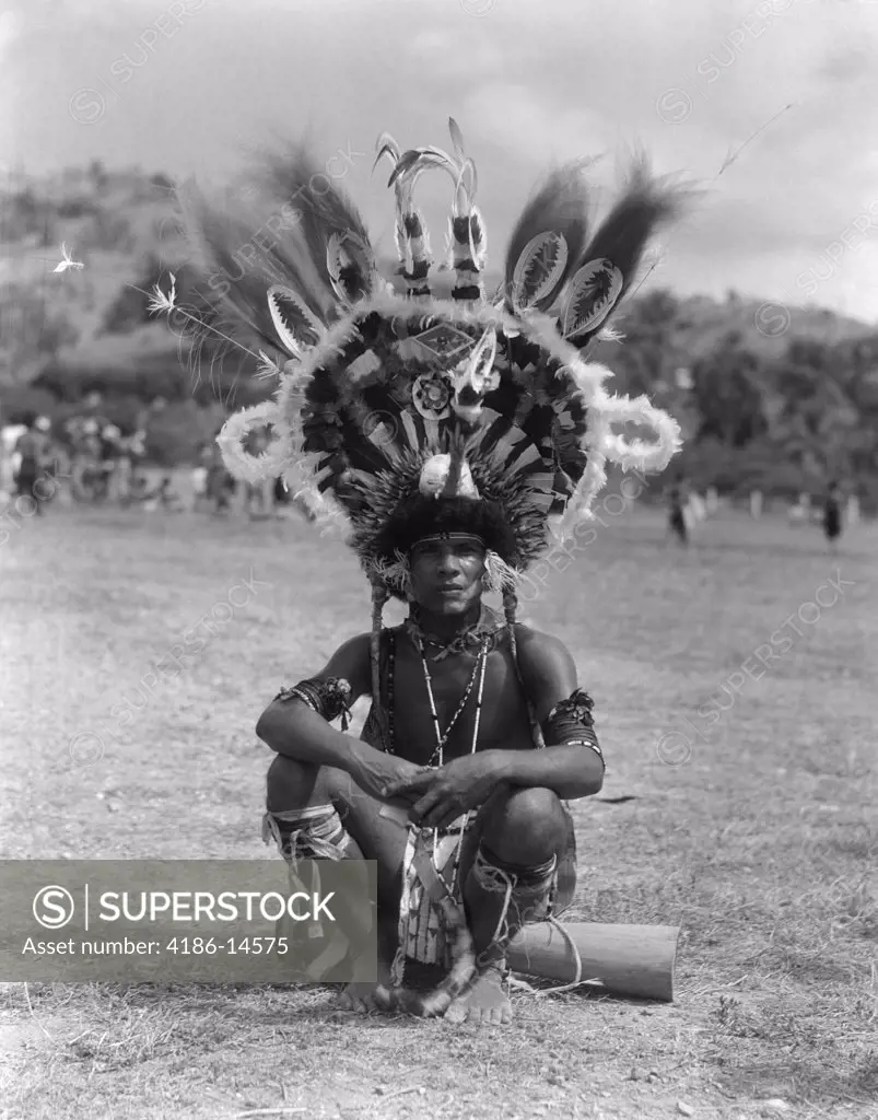 1920S 1930S Portrait Native Man In Elaborate Feathered Headdress Costume Sitting On Ground Port Moresby New Guinea