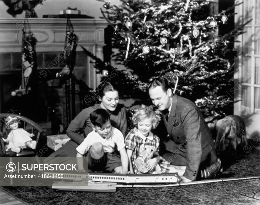 1930S Family Playing With Toy Train In Front Of Christmas Tree Fireplace