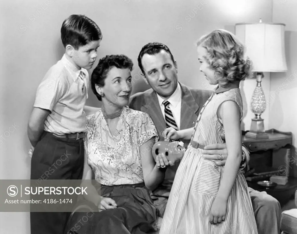 1950S Family Mother Holding Piggy Bank Daughter Dropping In Coin Father And Son Looking On