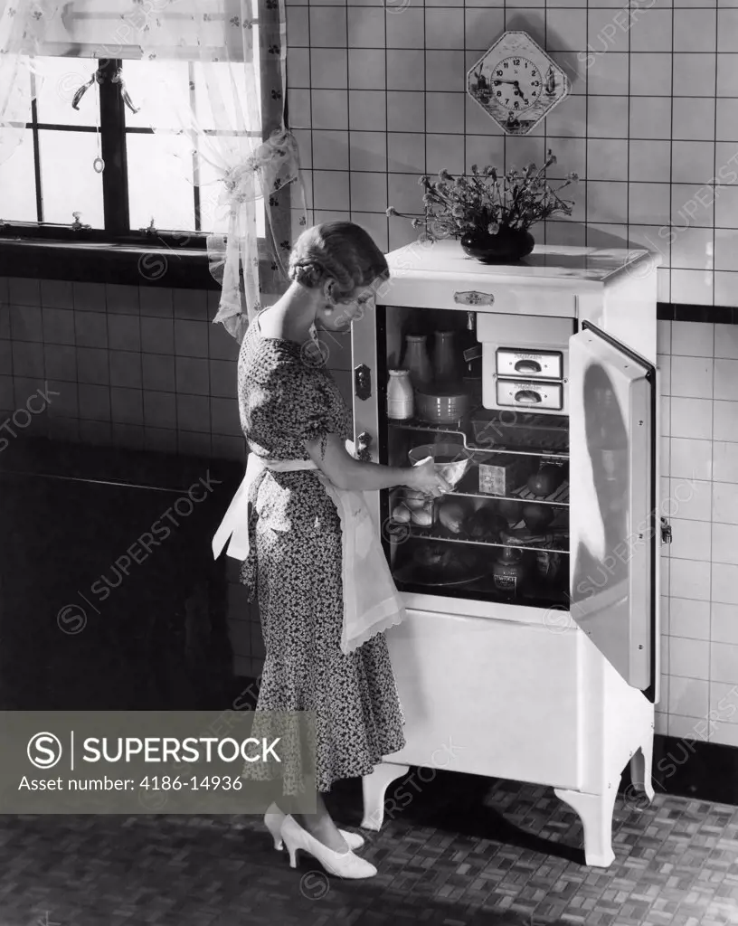 1920S 1930S Blond Woman In Apron Silk Party Dress High Heels Taking Dish From Electric Kitchen Refrigerator
