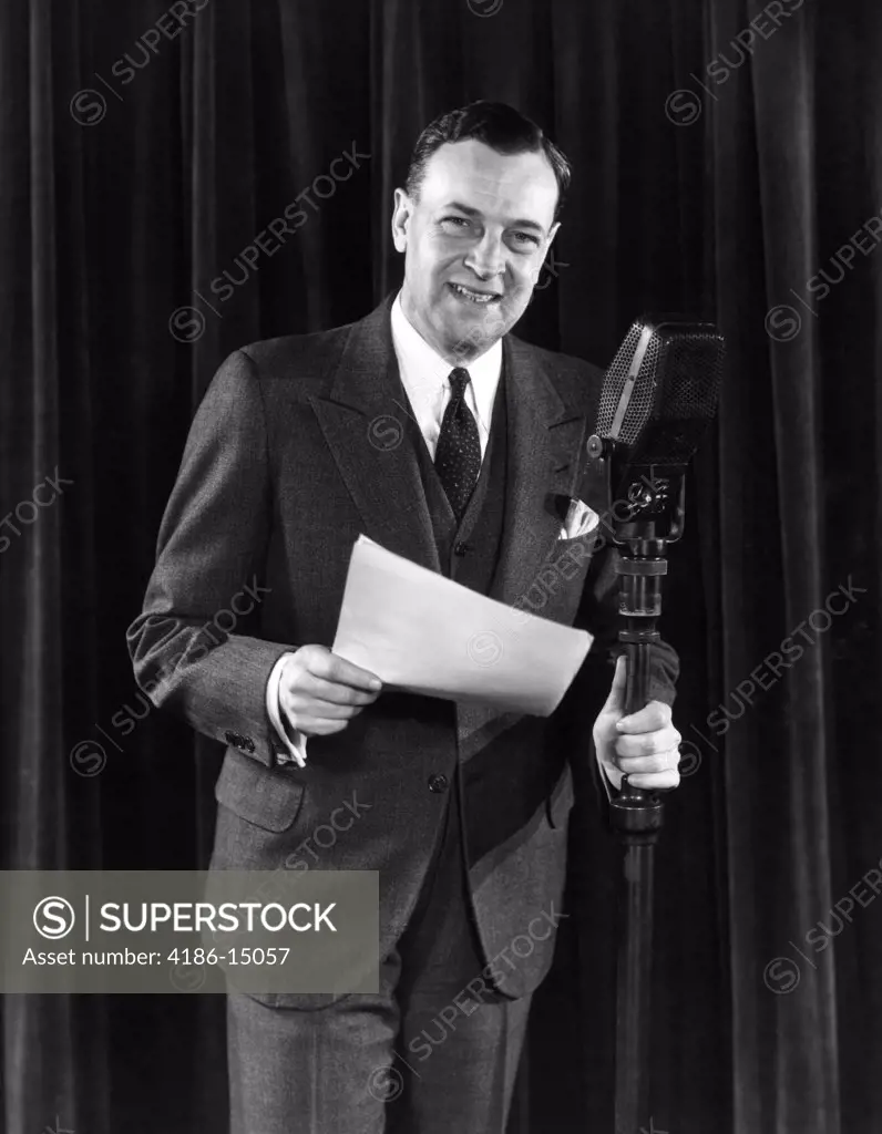 1940S Man Announcer Emcee Smiling Standing With A Script In One Hand The Other Holding The Microphone Stand Looking At Camera