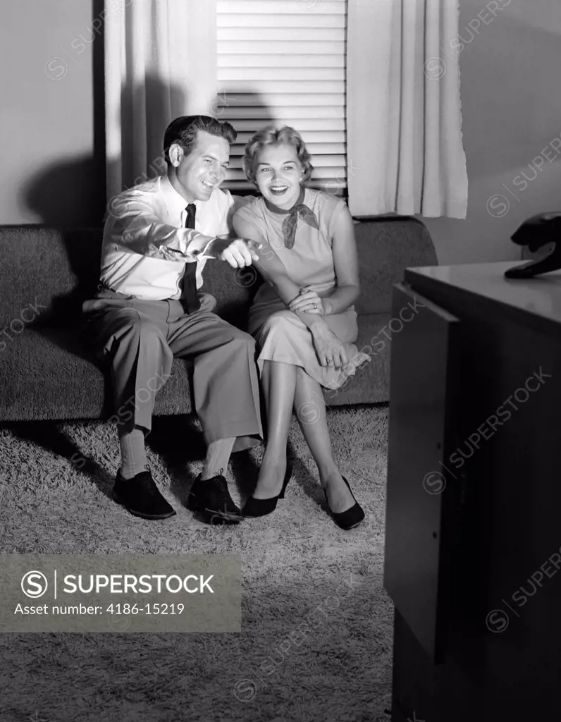 1950S Couple In Darkened Living Room Watching Tv With Husband Pointing At Screen