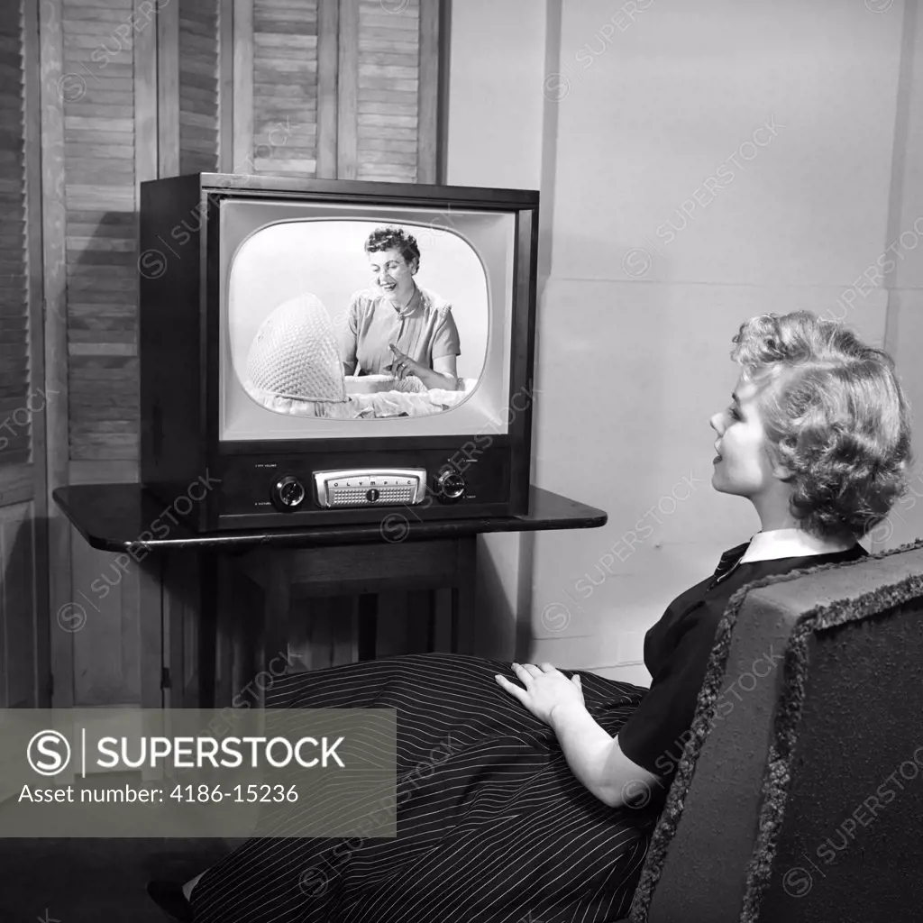 1950S Teen Sitting With Back To Viewer Watching A Woman Looking Into A Bassinet On Her Television In A Dark Room