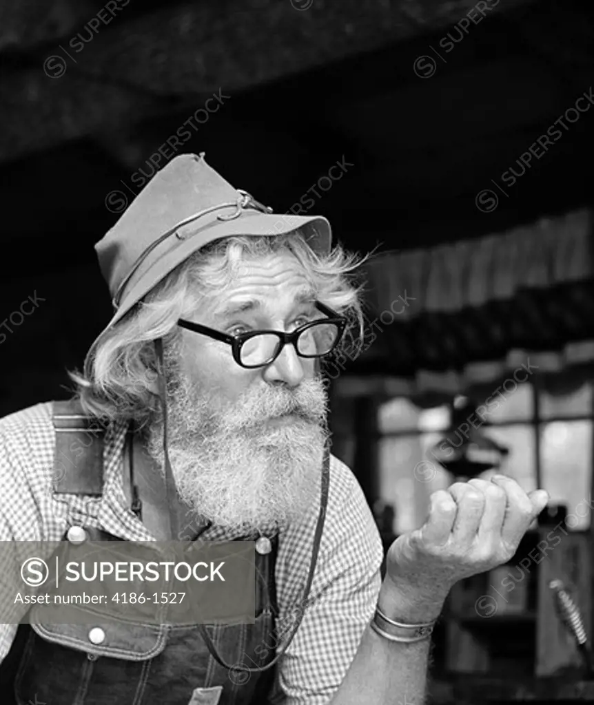 1970S Older Man Hillbilly Character Wearing Cloth Hat Overalls Gingham Shirt With Glasses Beard Outdoor