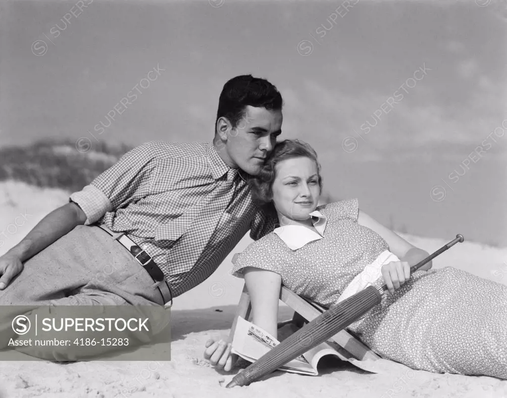 1930S Couple On Beach Woman Hold Closed Umbrella And Magazine Man Behind Face Touching Her Hair
