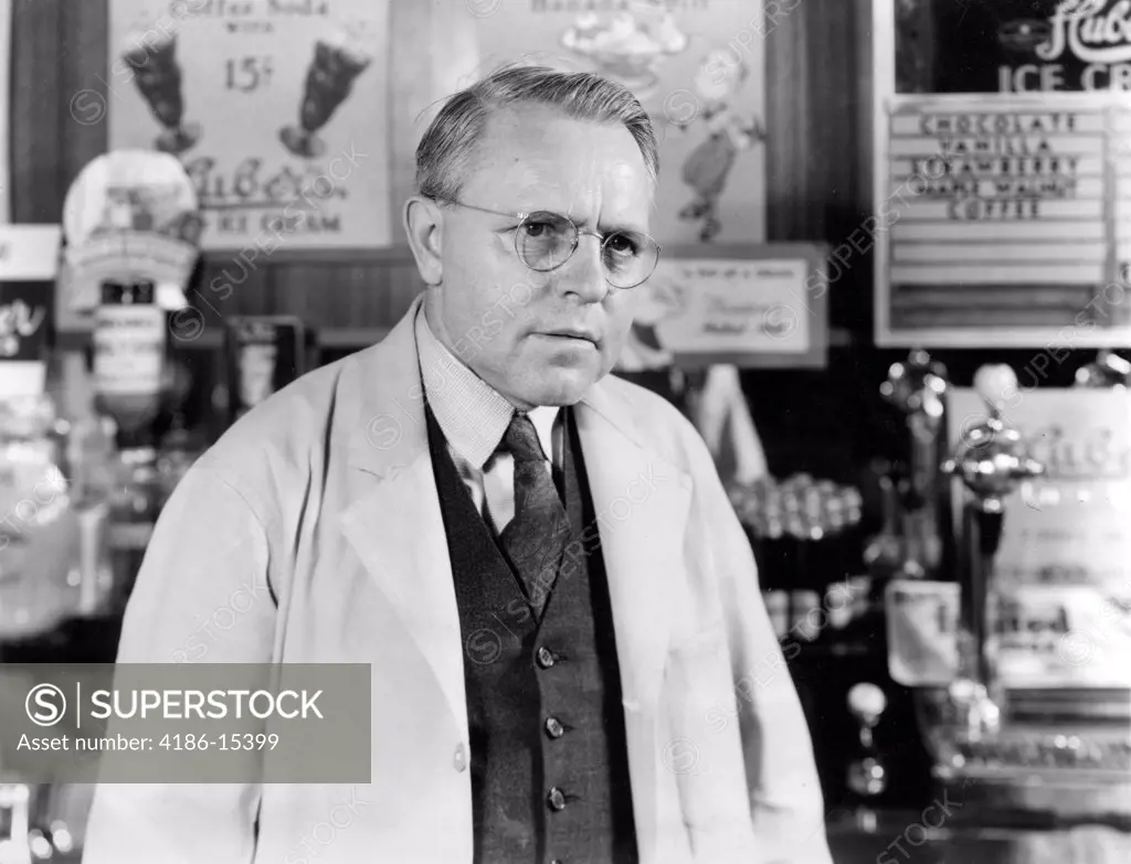 1930S 1940S Drug Store Soda Fountain Man Pharmacist Wearing White Coat And Glasses Listening