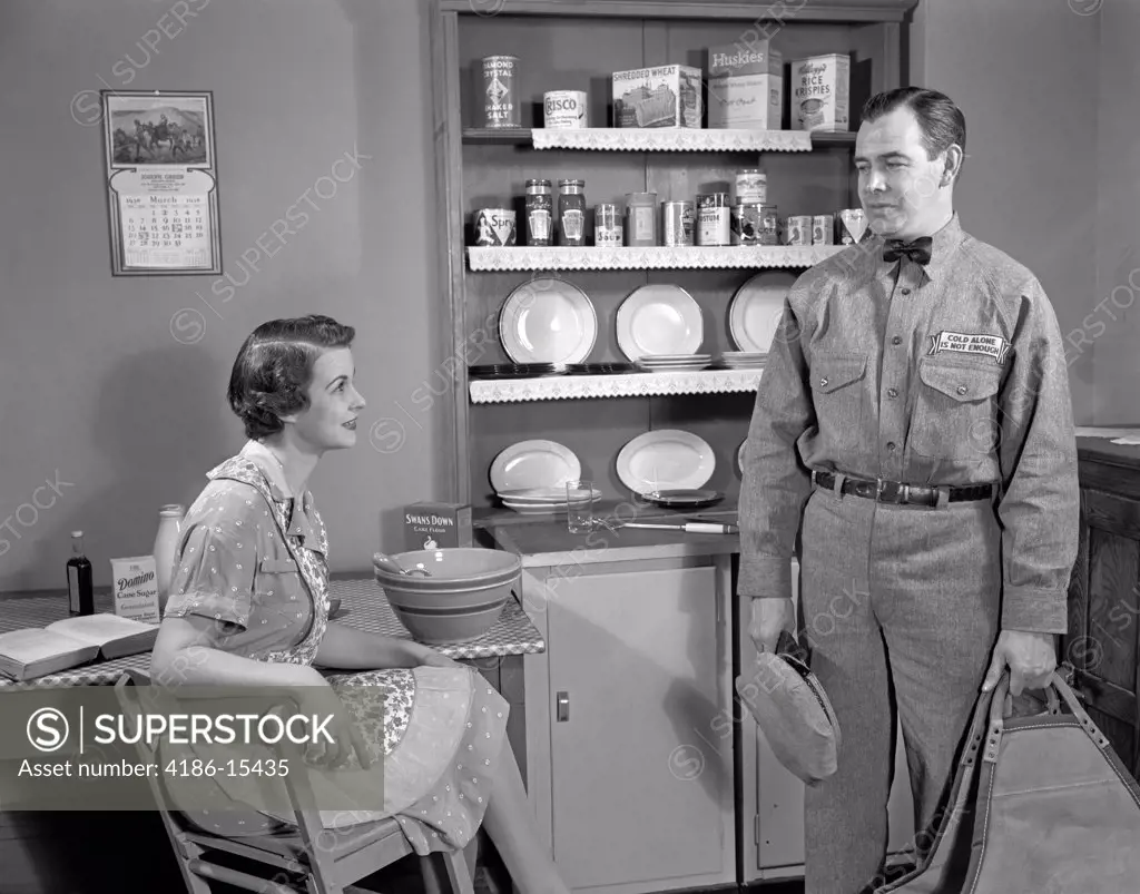 1940S Woman Apron Sitting At Kitchen Table Talking To Repairman Or Husband In Uniform Housewife Food Boxes On Shelves