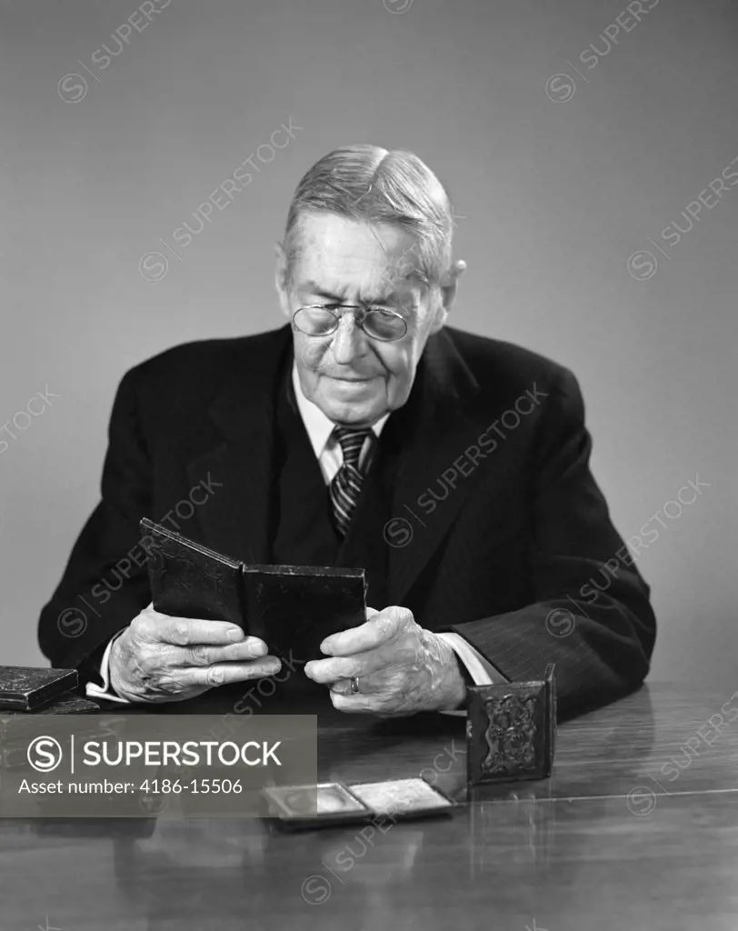 1940S Elderly Man Wearing Glasses Sitting At Table Looking At Daguerreotype Photographs