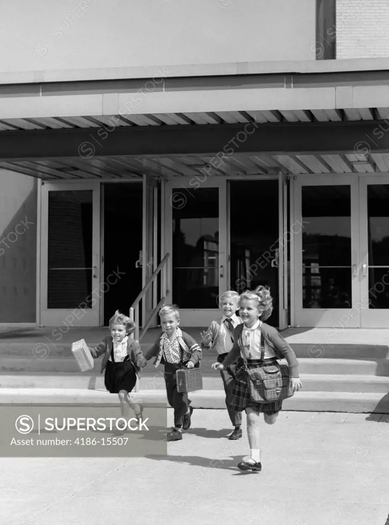 1950S Four Young Children With Bags And Lunchboxes Running From School Entrance Smiling Outdoor