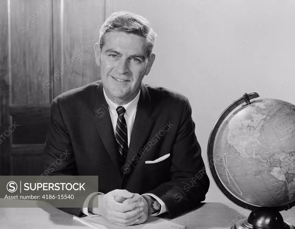 1960S Smiling Man Sitting At Desk With Earth Globe  