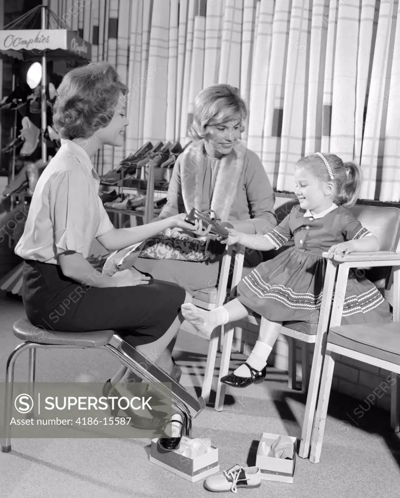 1960S Mother Daughter Shoe Shopping Saleswoman Showing Patent Leather Shoe To Girl In Retail Store