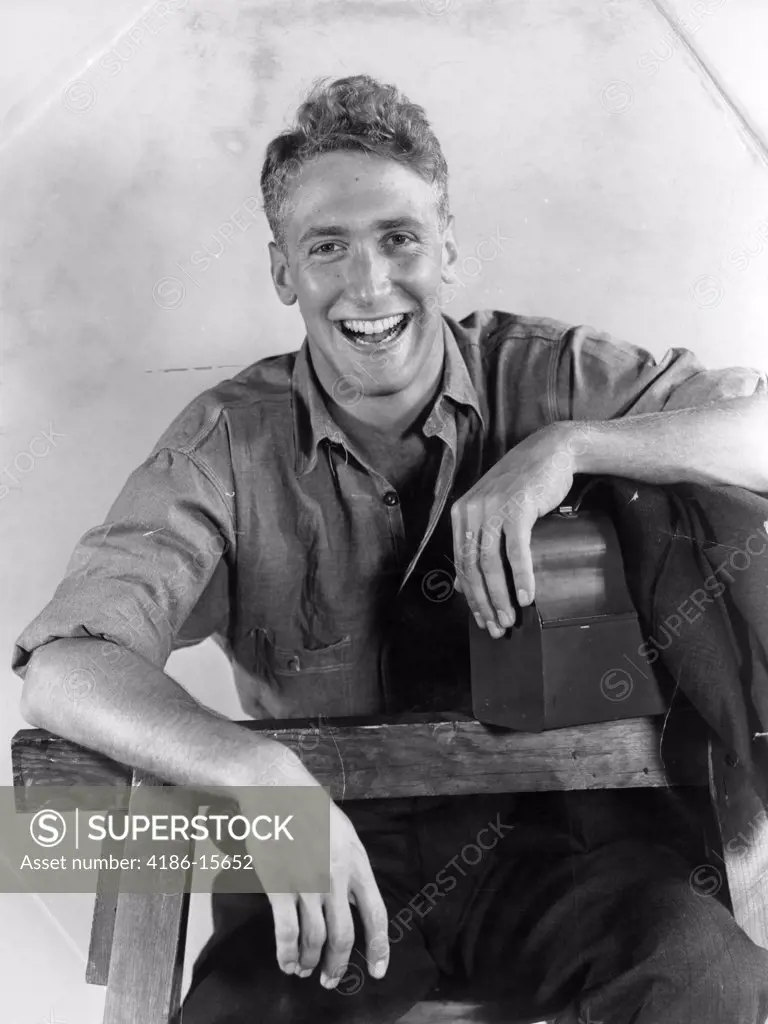 1940S Wavy Haired Smiling Young Man Wearing A Work Shirt Arm Resting On His Lunch Box And The Other On The Sawhorse