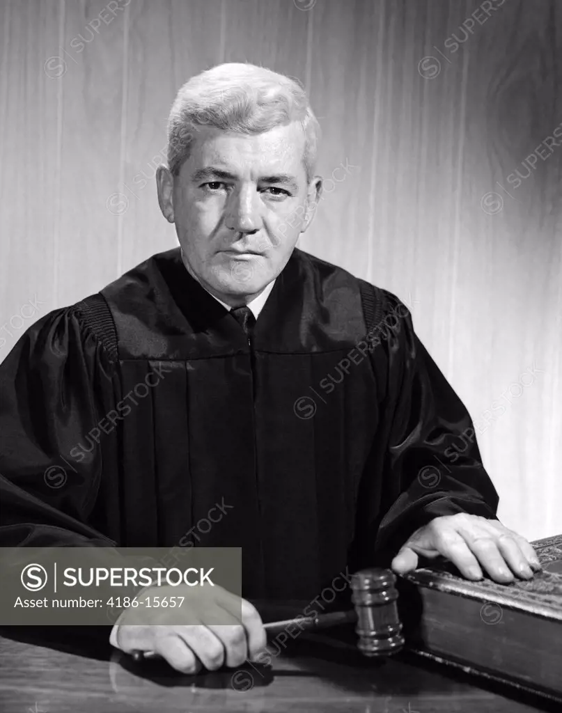 1960S Stern-Looking Judge Seated With Gavel In One Hand & Other Hand On Law Book