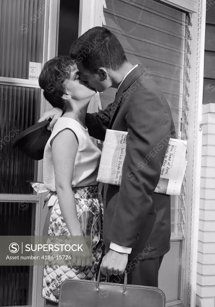 1960S Businessman With Newspaper & Briefcase At Door Of Home Kissing Wife In Apron Goodbye