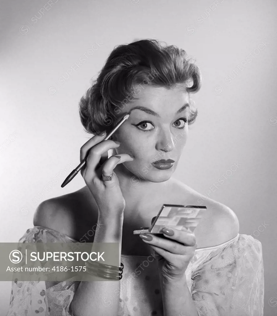 1950S 1960S Woman Looking At Camera Applying Makeup Eye Brow Pencil Holding Compact Mirror